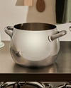 Polished stainless steel cooking pot by Alessi, featuring two handles and a rounded design, on a kitchen counter.
