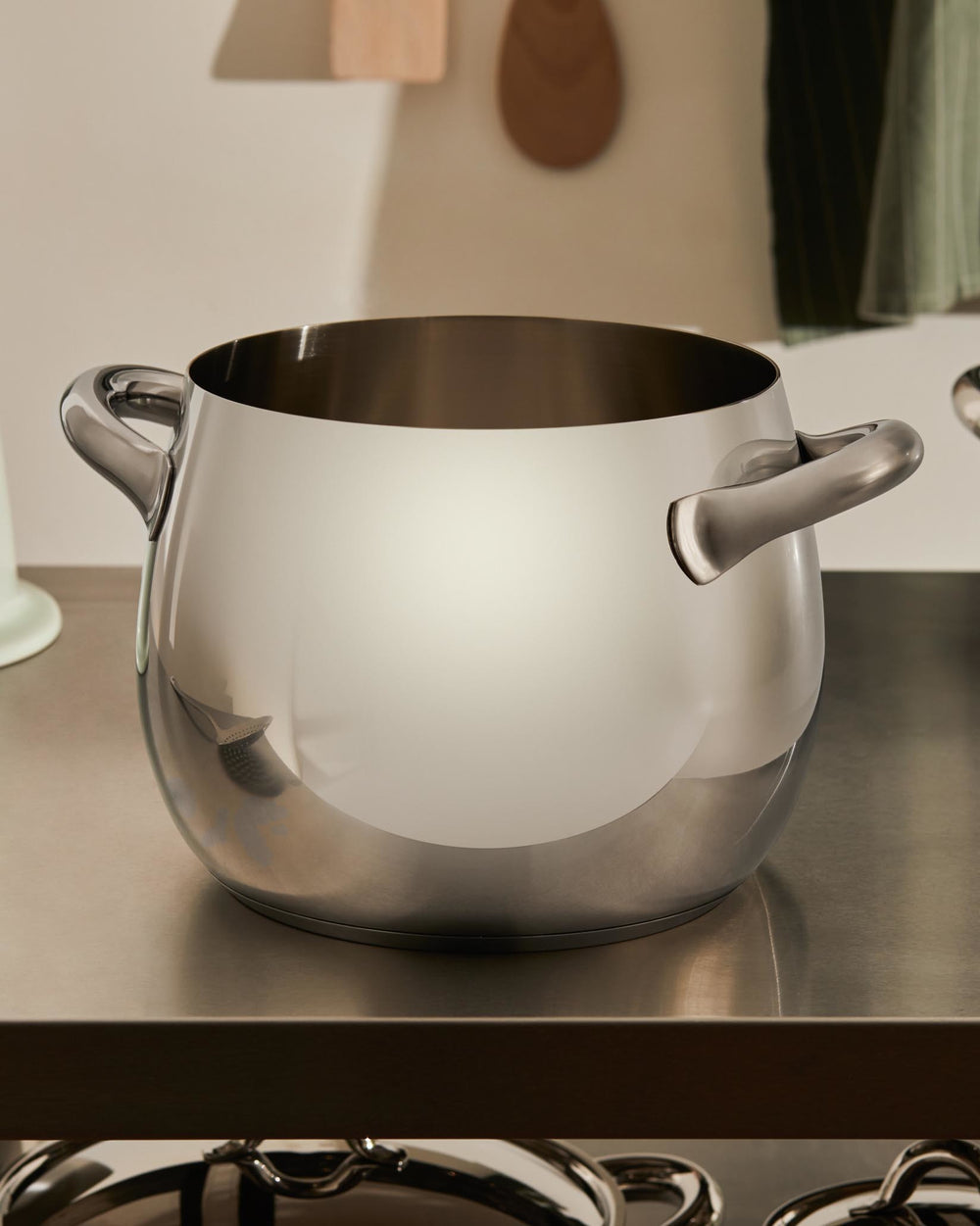 Polished stainless steel cooking pot by Alessi, featuring two handles and a rounded design, on a kitchen counter.