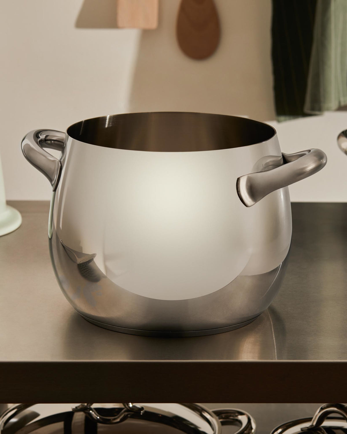 Polished stainless steel cooking pot by Alessi, featuring two handles and a rounded design, on a kitchen counter.
