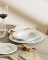 White, deep PlateBowlCup by Alessi, part of a table setting with wine and bread.