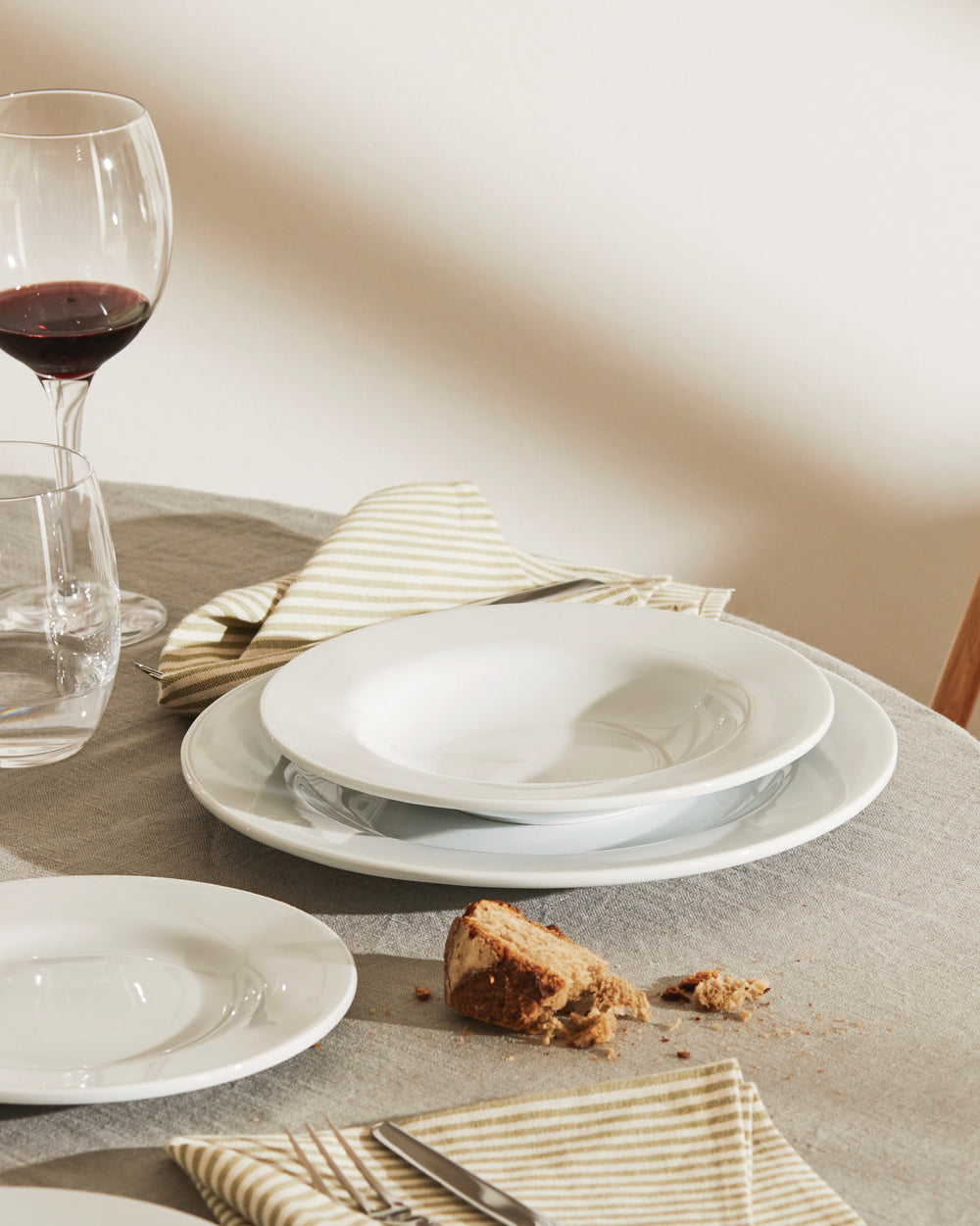 White, deep PlateBowlCup by Alessi, part of a table setting with wine and bread.