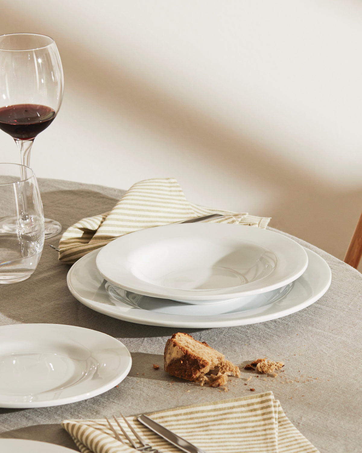 White, deep PlateBowlCup by Alessi, part of a table setting with wine and bread.