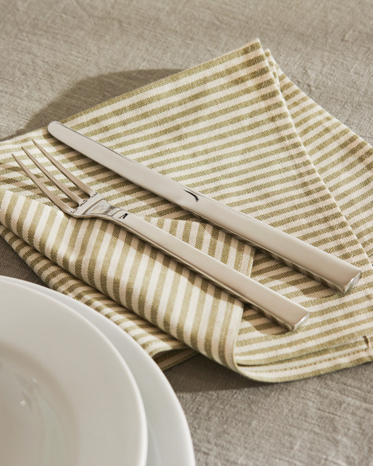 Sleek silver cutlery set by Alessi, featuring a knife and fork on a striped napkin next to white plates.