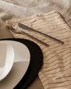 Colombina collection dining ware by Alessi, featuring modern black and white plates, silver cutlery, and a striped napkin.