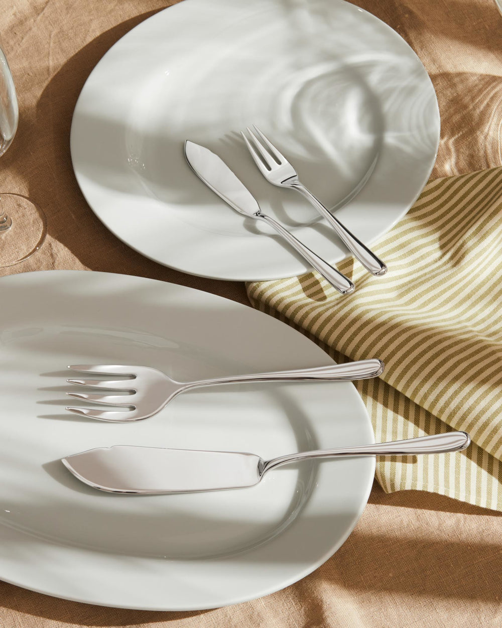 Silver flatware set by Alessi, featuring various forks and knives, displayed on white plates with a striped napkin.