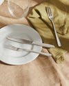 Caccia stainless steel cutlery by Alessi, with a knife and fork on a white plate and green linen napkin.