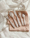 Silver stainless steel cutlery set by Alessi with embossed ornate handles, displayed on a pink napkin with plates.