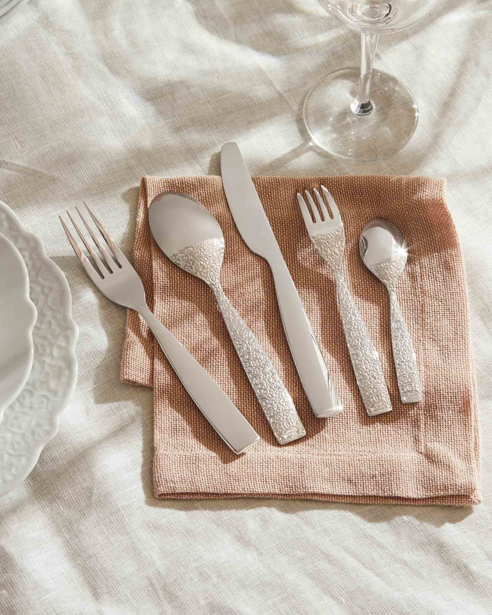 Silver cutlery set with ornate handles by Alessi, placed on a peach napkin and linen cloth.