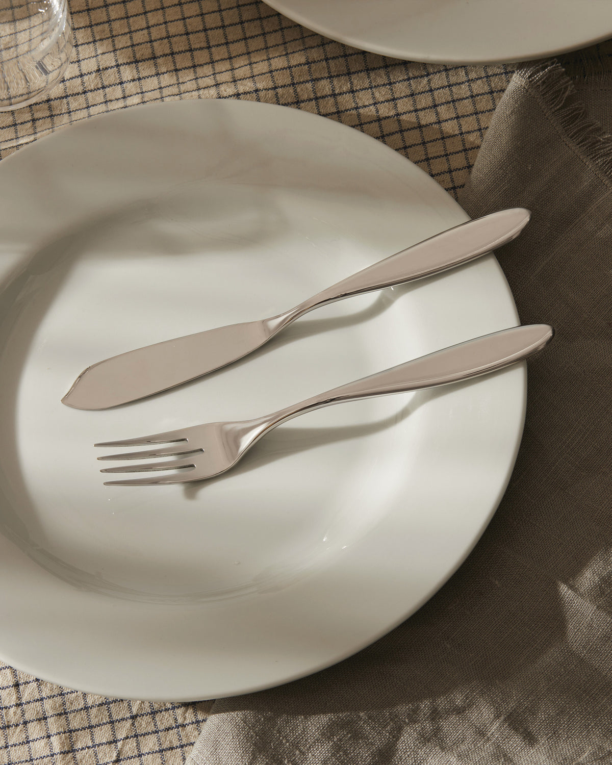 Mami white dinnerware by Alessi, with a silver fork and knife, on a checkered tablecloth and linen napkin.