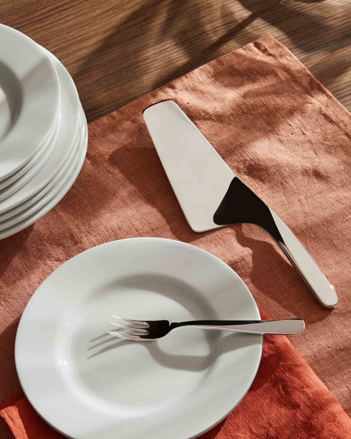 Sleek silver cake server by Alessi with black handle detail, resting on a textured orange napkin with a white plate.