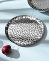 Silver metallic platter by Alessi with a faceted geometric pattern, next to a red apple.