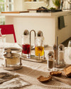 Polished silver and clear glass salt and pepper shakers by Alessi, with matching toothpick holder and cruets on a checkered table.