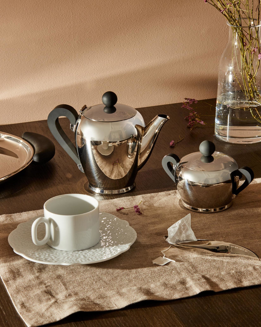 Polished stainless steel Bombé teapot by Alessi, with black handles and knob, displayed with a matching sugar bowl.