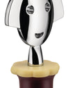 Chrome bottle stopper with a stylized smiling face by Alessi, featuring a yellow wavy base partially inserted into a dark bottle.