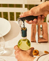 Black and silver parrot corkscrew by Alessi uncorking a white wine bottle at a table.