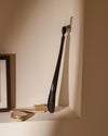 Black glossy shoehorn by Alessi with a brown leather loop, hanging on a wall above shoe polish and a brush.