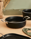 Black non-stick cookware set by Alessi with silver handles, featuring a prominent round casserole dish and grill pan.