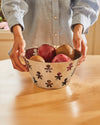 Polished metal fruit bowl by Alessi, featuring a cut-out 'Girotondo' human figure pattern, filled with fruit.