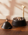 Black dog bowl and treat jar set by Alessi, featuring a bone-shaped stand and a white dog figurine.