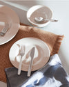 Itsumo stainless steel cutlery set by Alessi, arranged on white dinnerware with a woven placemat and blue napkin.