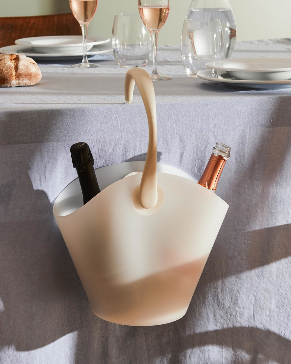 White Chiringuito Cooler by Alessi, holding two bottles on a light blue linen table setting.