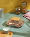 Translucent biscuit box by Alessi with an irregular shape and a cream-colored, biscuit-shaped lid, filled with cookies.