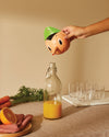 Orange and green Pinocchio-shaped citrus juicer by Alessi, pouring juice from its nose into a bottle.