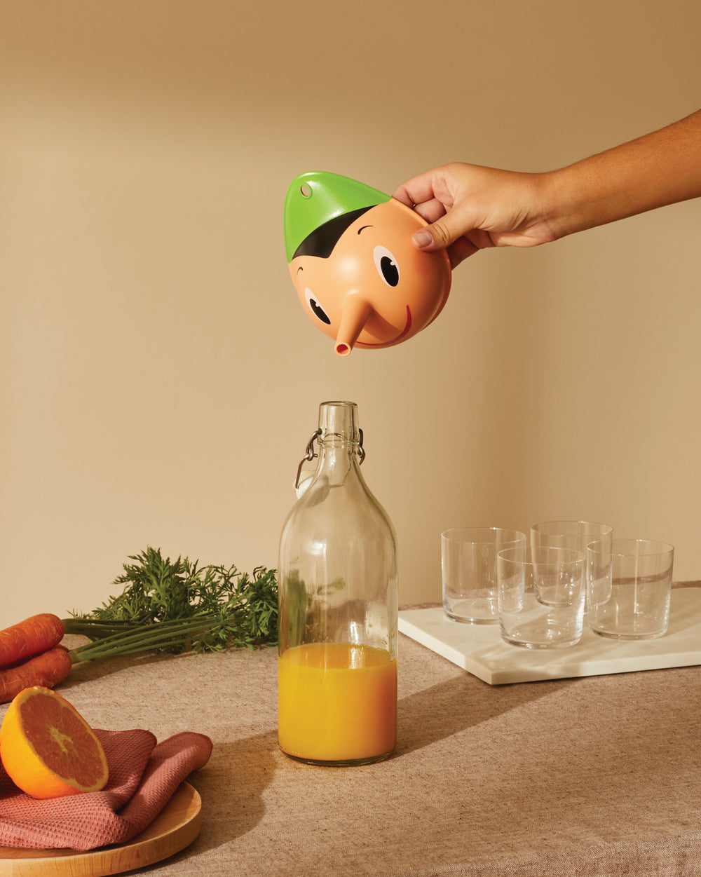 Orange and green Pinocchio-shaped citrus juicer by Alessi, pouring juice from its nose into a bottle.