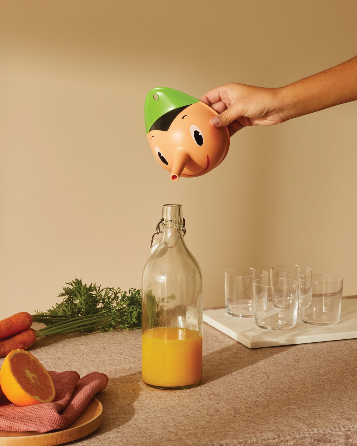 Orange and green Pinocchio-shaped citrus juicer by Alessi, pouring juice from its nose into a bottle.