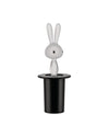 White translucent rabbit figurine by Alessi, with black eyes and long ears, emerging from a matte black top hat.