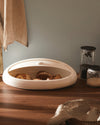 Oval white Gnam bread bin by Alessi, a modern design open with bread inside on a wooden counter.