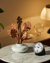 Black and white alarm clock by Alessi with a round face and silver bezel, tilted on a marble table.