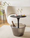 Black pedestal drinks table with smoky ribbed plastic cooler by Alessi, holding champagne and ice, with glasses and macarons.