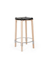 Black contoured stool by Alessi with light wood legs and a circular silver footrest, front view.