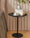 Black Op-la side table by Alessi, with cut-out handles, styled with stacked books and a white cup.