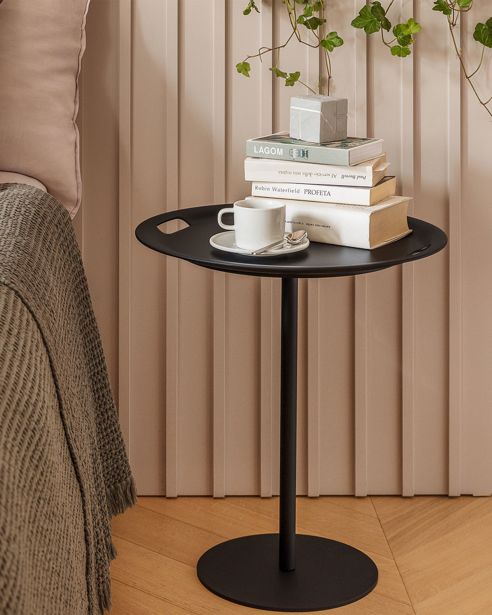 Black Op-la side table by Alessi, with cut-out handles, styled with stacked books and a white cup.