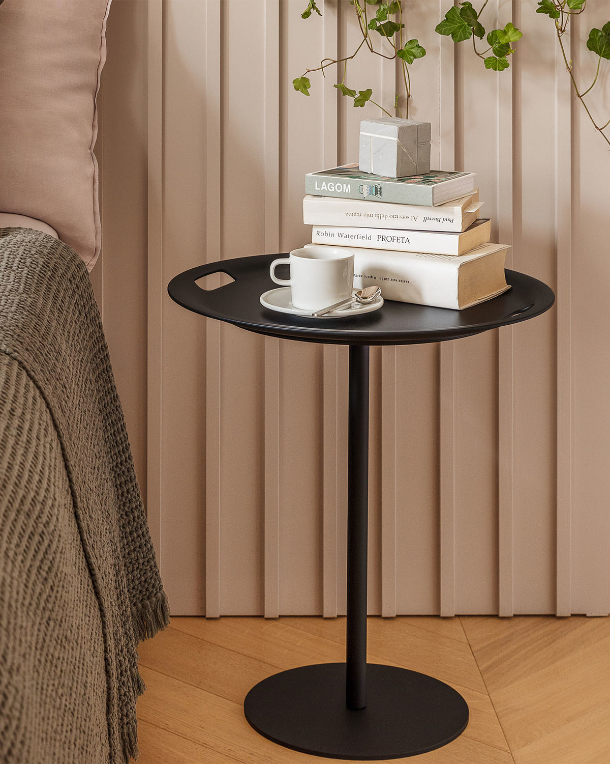 Black Op-la side table by Alessi, with cut-out handles, styled with stacked books and a white cup.