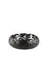 Black metal decorative bowl by Alessi with intricate organic bark-like cutouts, angled view.
