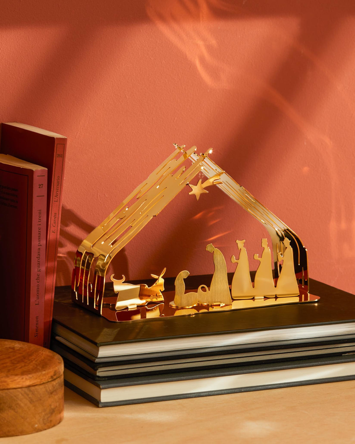 Golden laser-cut Bark Crib by Alessi, depicting a nativity scene with figures, resting on dark books.