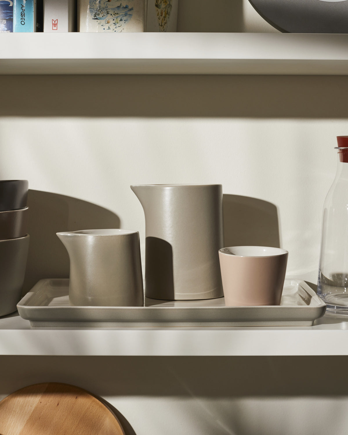 Beige ceramic tableware set by Alessi, with two pitchers, a light pink cup, and a rectangular tray.