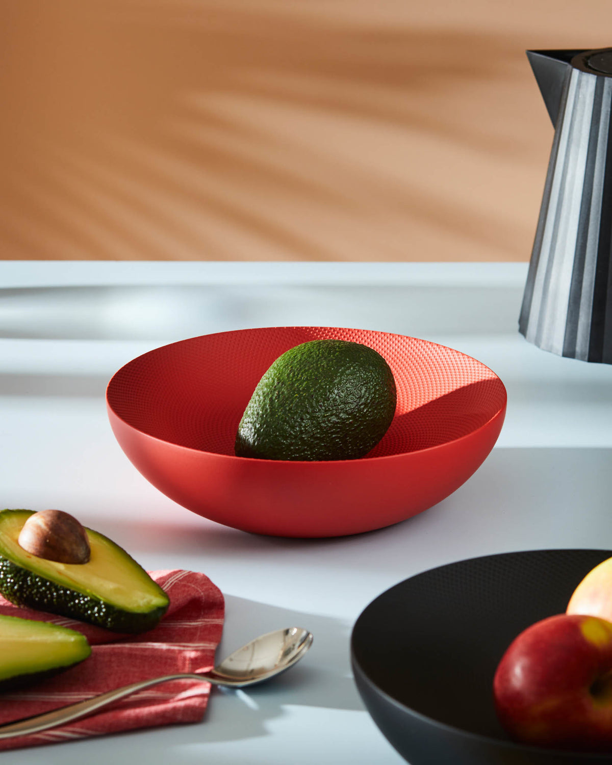 Red textured fruit bowl by Alessi with a dimpled surface, holding a green avocado.