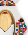 Golden egg-shaped Holyhedrics Jesus by Alessi in a white holder with colorful geometric pixel patterns.