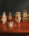 White geometric Holyhedrics Mary figure by Alessi with a golden halo and vibrant multicolored pixelated patterns, alongside other matching figures and books on wood.