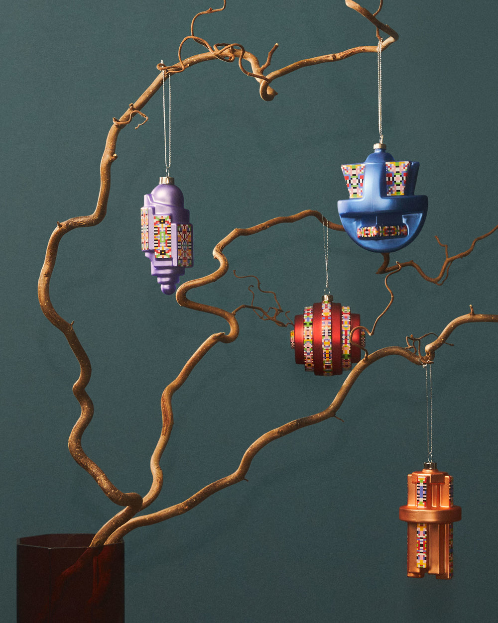 Purple arch-shaped Christmas tree ornament by Alessi with colorful pixelated geometric patterns hanging from a branch.