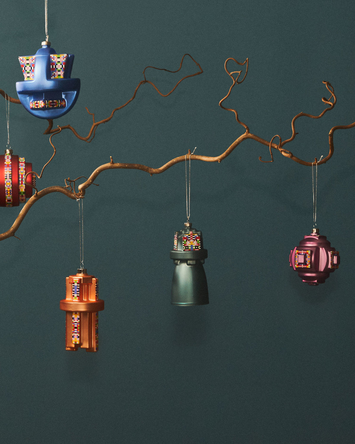 Assorted Holyhedrics Prism Christmas tree ornaments by Alessi with pixelated patterns, hanging from a bare branch.