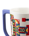 White mug by Alessi with a purple handle and a colorful pixelated geometric pattern, cropped view.