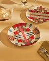 Two white plates by Alessi with a bold, colorful geometric pattern, on a table with desserts.