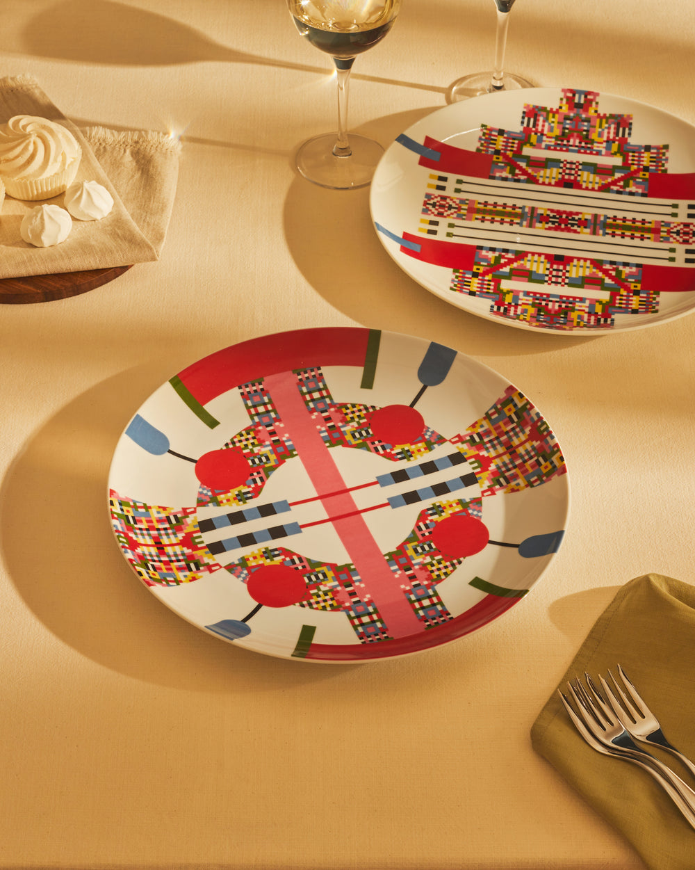 Two white plates by Alessi with a bold, colorful geometric pattern, on a table with desserts.