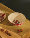 White ceramic bowl by Alessi with colorful abstract geometric pattern and red circles, on an olive green tablecloth with walnuts.