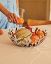 Stainless steel fruit bowl by Alessi, featuring an intricate coral design, being filled with colorful fruits by a hand in a blue dress.